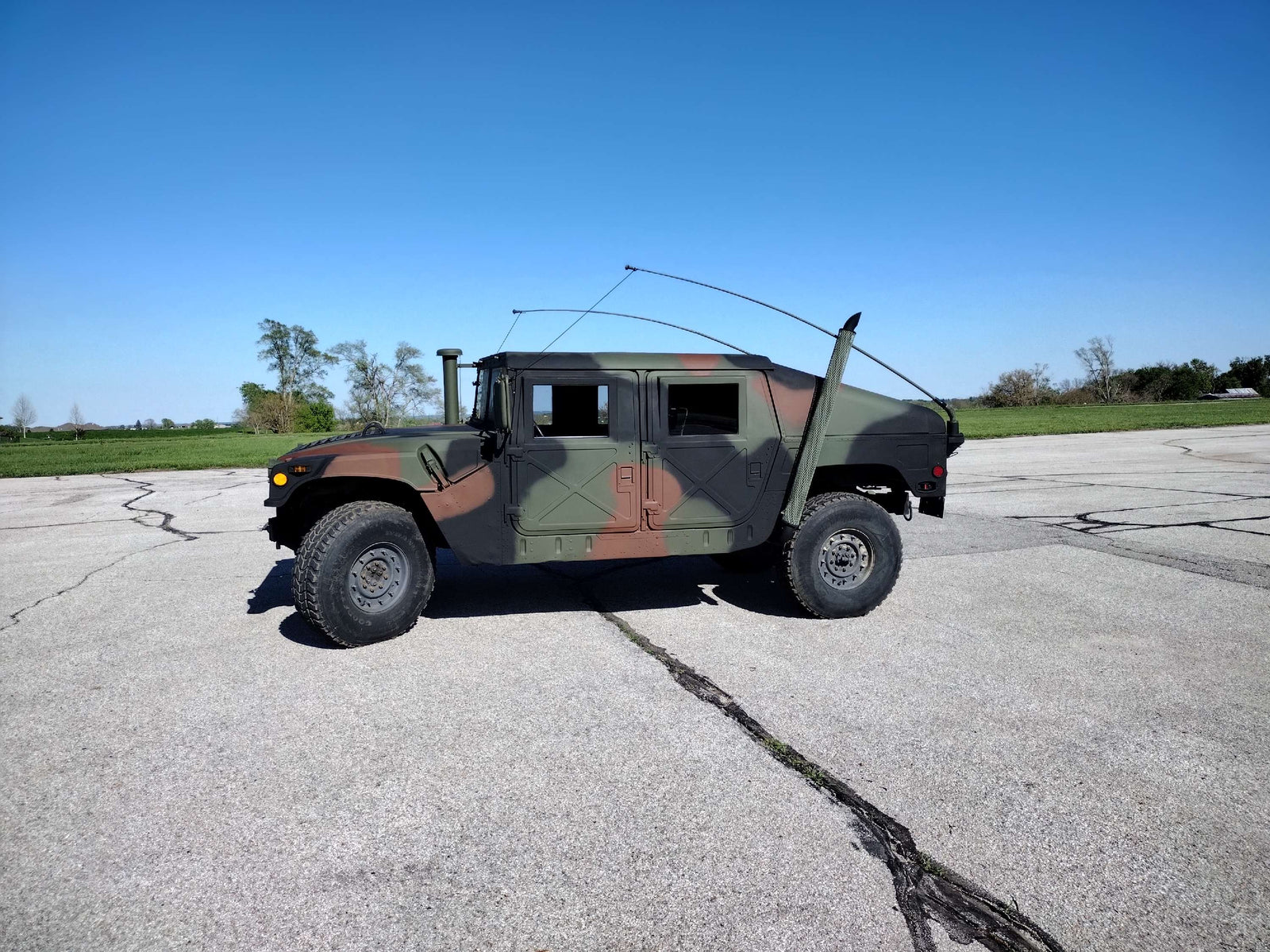 Woodland-camouflage HMMWV in left profile with the whip antenna raised