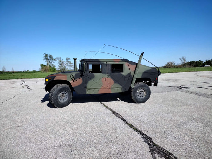 Woodland-camouflage HMMWV in left profile with the whip antenna raised