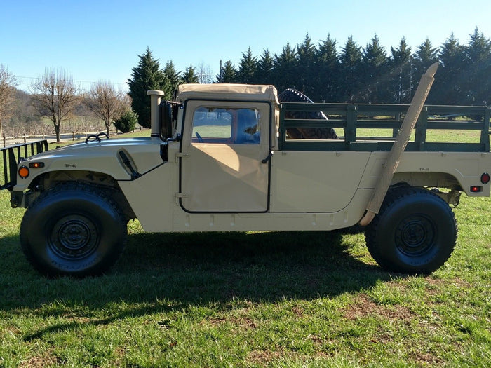 Tan HMMWV troop carrier with a drop-side cargo bed, left profile on grass
